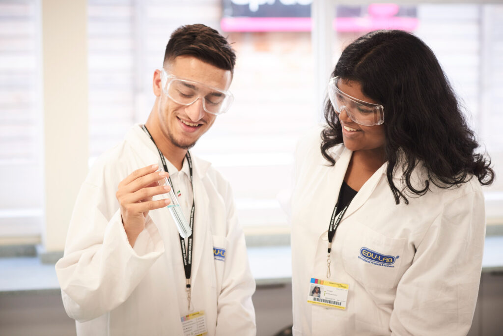 2-students-in-lab-coats-looking-at-test-tubes