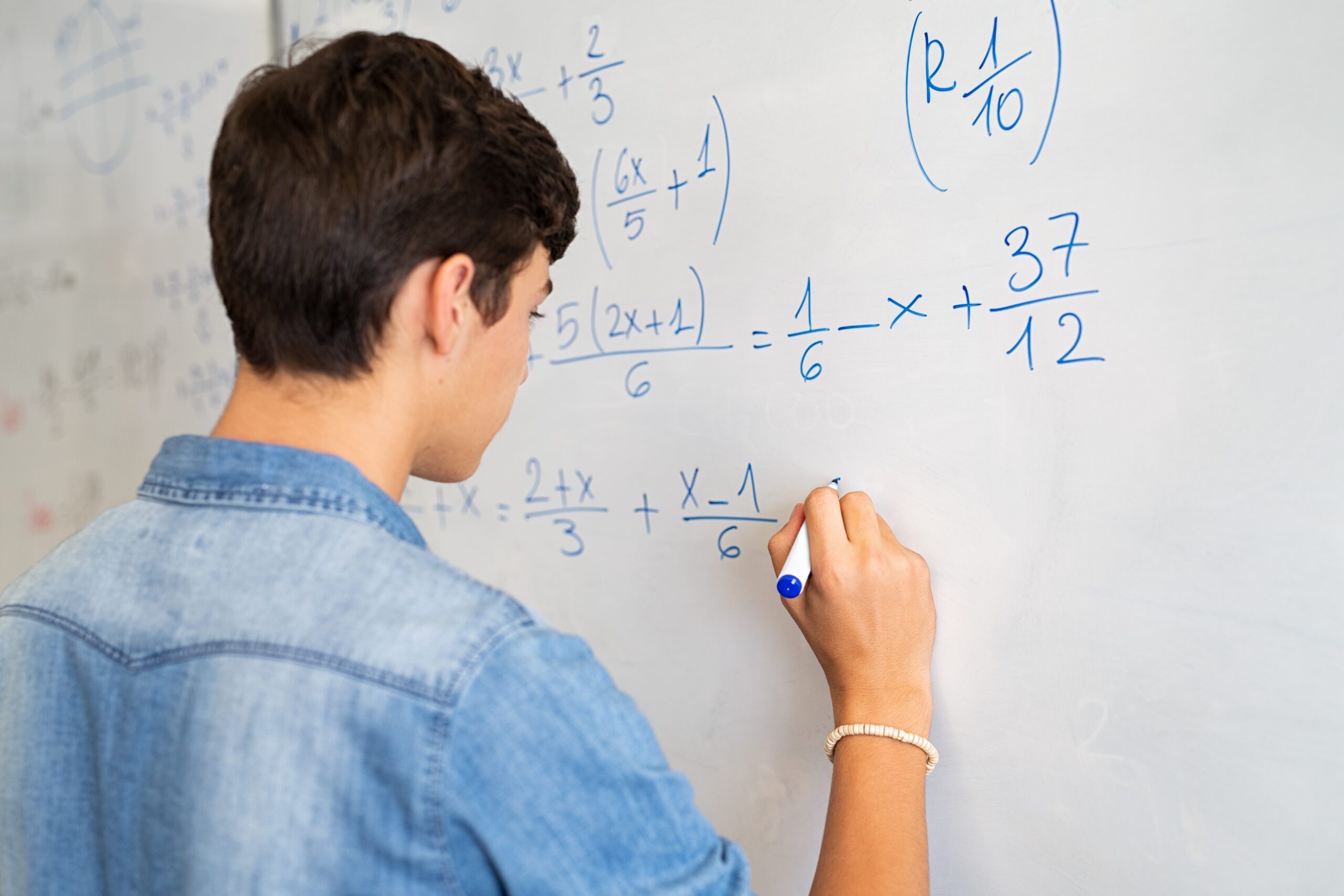 Stanmore College - Maths. Back view of student solving math problem on whiteboard in classroom.