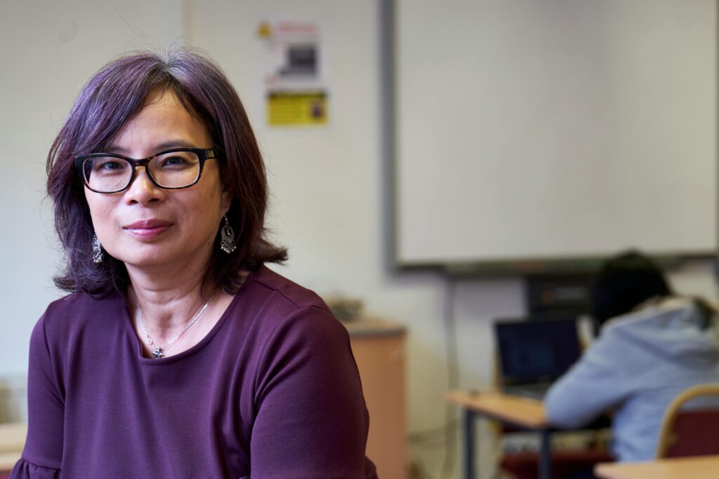 pexels-photo-13804486-13804486 Asian woman with glasses and purple hair seated in a classroom, exuding confidence.