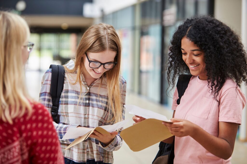 Stanmore College - Certificate Collection. Three girls huddled, smiling and looking at their results